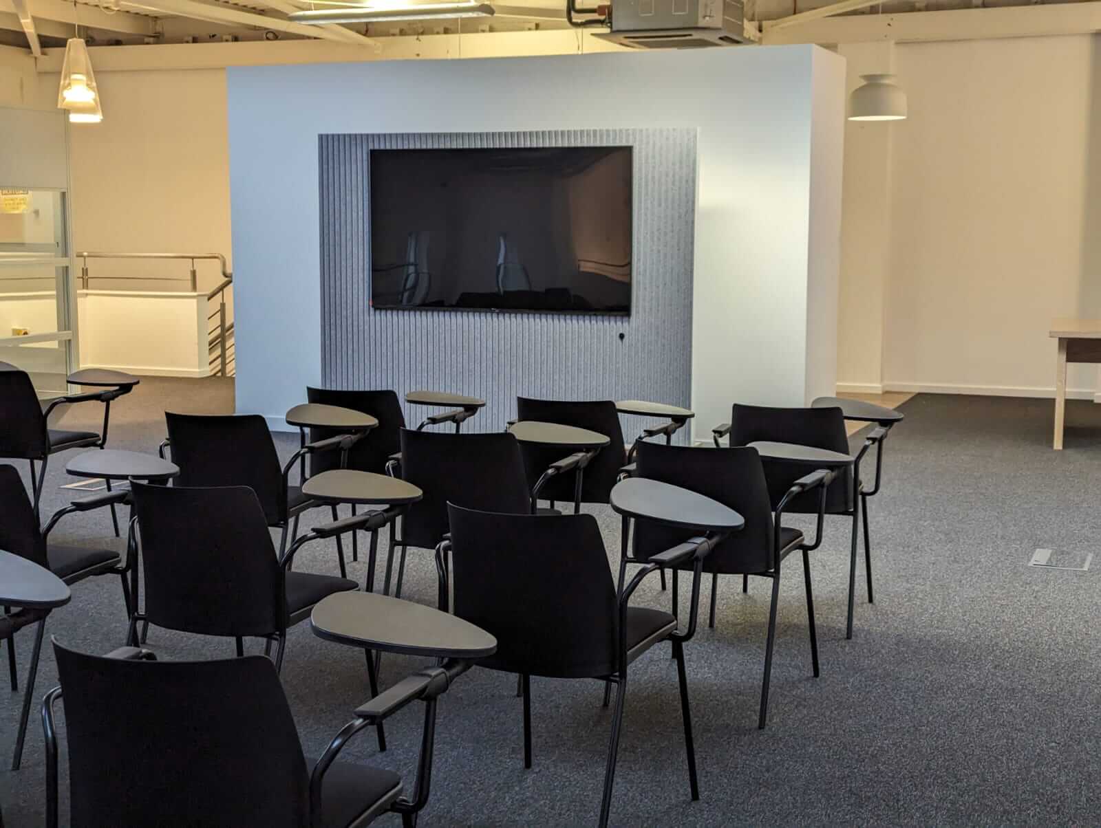 Digital screen surrounded by acoustic panel in a room set up with rows of chairs for a lecture or conference